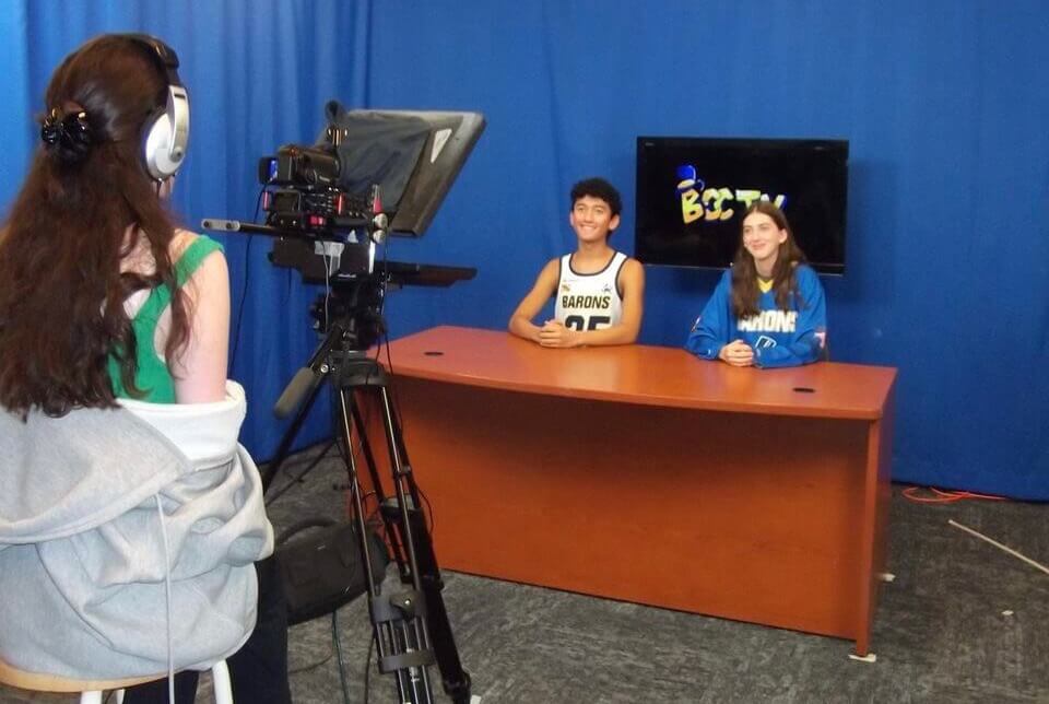 Two students are filmed by one of their peers for their school's TV station